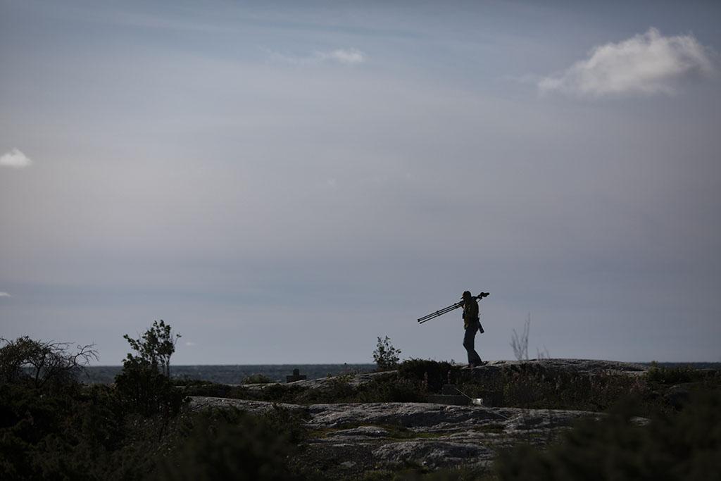 Valokuvaaja kantaa kameraa merellisellä kalliolla.