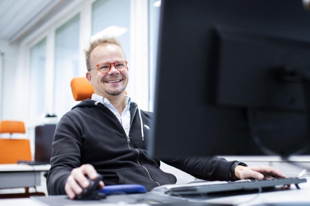 Mies istuu työpöydän ääressä tietokoneella, kädet hiirellä ja näppäimistöllä.